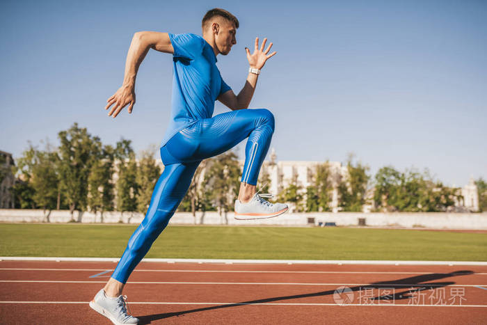 活跃的年轻男性运动员在阳光明媚的日子里独自沿着体育场的赛道跑步和