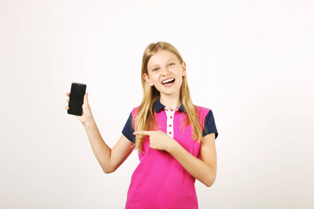 休闲青少年女孩的肖像，有长长的天然金发食指指向空白屏幕手机。 快乐的年轻女性持有智能手机显示显示。 白色背景拷贝空间
