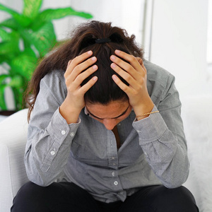 在家沙发上患有头痛偏头痛的女人。 健康问题压力和抑郁。 关闭办公室工人妇女头痛。 女性用手抱着头。