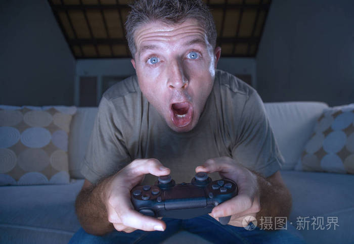 生活方式肖像年轻英俊兴奋的男人在家里客厅玩电子游戏,在沙发沙发上