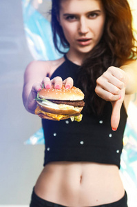 女孩拒绝吃汉堡。 健康的生活方式概念。 垃圾食品的概念。 拇指向下汉堡。 女孩不喜欢手