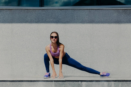 人们的灵活性和拉伸概念。 活跃的年轻运动女性试图保持健康和良好的形状，穿阴影和运动鞋在慢跑锻炼前户外热身。
