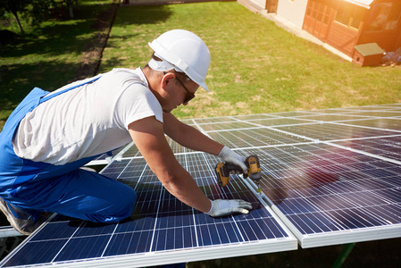专业工人在绿色金属建筑上安装太阳能电池板，使用不同的设备戴安全帽。 创新的能源解决方案。 使用可再生资源。 绿色能源。