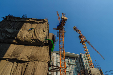 在高层建筑中，在公寓建筑工地上，在钢框架上安装了起重机械塔吊。摩天大楼的建造与塔吊顶在戏剧性的天空背景下。