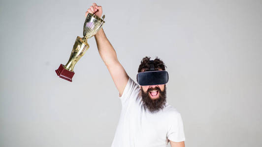 在线锦标赛。在虚拟现实游戏中感到胜利。取得胜利。时髦的虚拟玩家获得了成就。男子胡子时髦 vr 耳机持有金色酒杯。人优胜者虚拟竞争