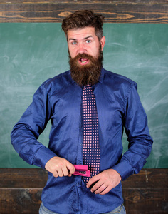 学校事故预防。老师胡子的人与粉红色订书机的黑板背景。学校文具。人邋遢使用订书机危险的方式。时髦老师正式佩带领带举行订书机