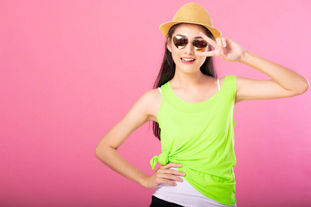 一个微笑迷人的女人的肖像，穿着绿色的夏季服装和帽子，摆着胜利标志，站着看着独立于粉红色背景的相机。