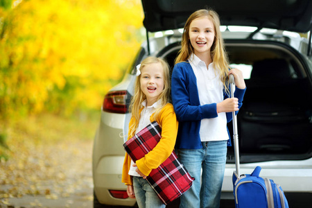 两个可爱的女孩带着一个手提箱和他们的父母一起度假。 两个孩子期待着一次公路旅行或旅行。 学校的秋假。 家庭乘车旅行。