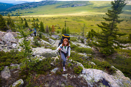 山脉中的大气时刻。 徒步旅行妇女与背包旅行者在山顶。 时尚的女人在背景下徒步旅行，绿色的森林田野和高山