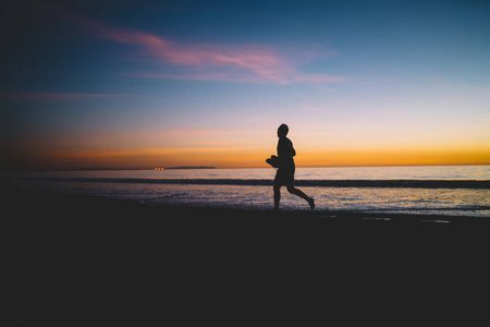傍晚时分,在沙滩上奔跑的年轻人剪影在夕阳西下的沙滩上慢跑,在海上的