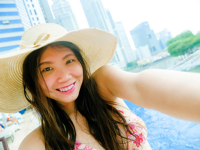 年轻快乐美丽的亚洲韩国旅游女性，在豪华酒店无限泳池，用手机相机自拍，现代建筑，城市背景，旅游度假理念