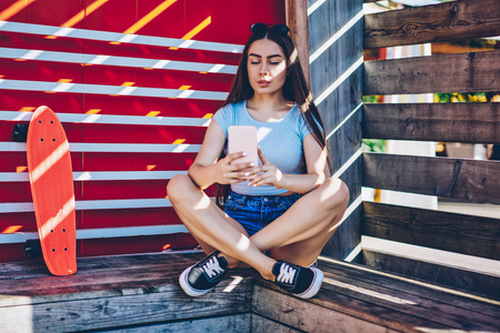 美丽的女性爱滑板，坐在莲花外面，通过4g互联网连接在智能手机上安装新的照片应用程序。迷人的博主为户外休息的网络做自拍。