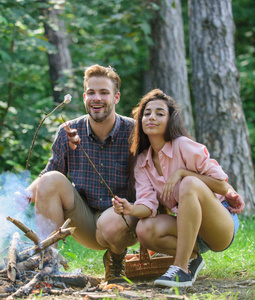 夫妇烤香肠在棍子自然背景。情侣喜欢野营森林烧烤香肠在篝火。传统的烘焙食品作为野餐的属性。野营和野餐