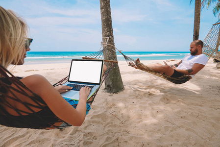 在热带岛屿的沙滩上远程工作时，女性自由职业者在上网本键盘上输入文本，并在空白屏幕区域为您的网站输入文本。