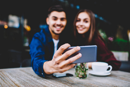 有选择地把注意力集中在智能手机上，年轻人和女朋友坐在咖啡馆的露台上，摆出一副自拍的姿势，让快乐的男性和女性嬉皮士用手机在网络上拍