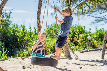 两个金发小男孩在热带沙滩荡秋千上玩得很开心