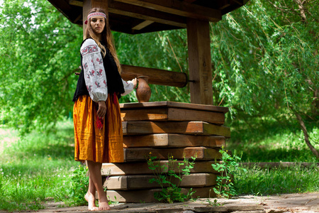 美丽纤细的乌克兰人在木制水井的背景上刺绣，获得淡水