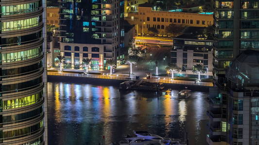 美丽的鸟瞰迪拜码头长廊和运河与浮动游艇和船在迪拜阿联酋。 照亮了现代塔楼，道路上闪烁着灯光和交通。