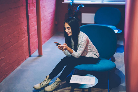 年轻的白种人女同事在满足无线连接要求的手机上安装应用程序时，在空闲时间在网络中和通过智能手机阅读新闻