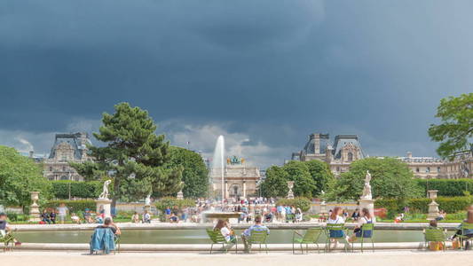 人们在卢浮宫附近的杜伊莱里宫露天公园喷泉放松。 查看背景中的旋转弧。 夏日的景象与多云的蓝天。 法国巴黎