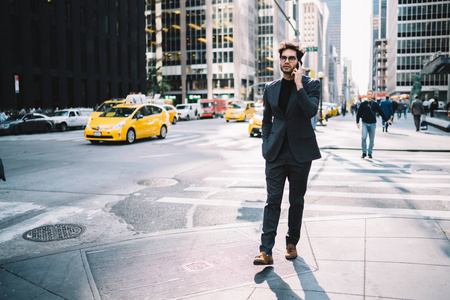 自信自豪的首席执行官漫步在纽约街头，在智能手机上与商业伙伴交谈，讨论最后的金融新闻。成功的经济学家穿着时尚的正式服装，在电话上交