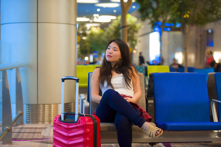 年轻快乐美丽的亚洲旅游女性，坐在机场登机口，手提行李在假期中等待航班