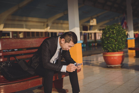 工作失望亚洲商人坐在火车站,低头看手机屏幕,感到金融危机的压力和