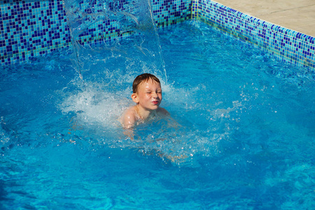 快乐的孩子在海边的一个热带度假胜地游泳池的蓝色水中玩耍。 暑假概念。 可爱的男孩在游泳池里游泳。 在游泳池里嬉戏玩耍