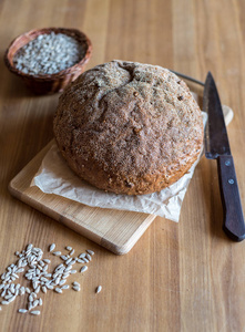 新鲜烘焙的自制面包在木板上，刀和葵花籽在桌子上选择性聚焦。 砧板上的乡村圆面包。 乡村风格。 还活着