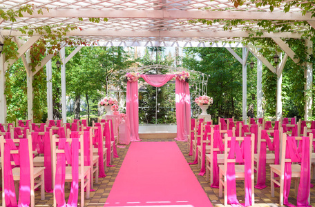 婚礼仪式用粉红色的地方，婚礼拱门上装饰着鲜花粉红布和木制椅子，供户外两边的客人使用。 漂亮的结婚拱门，两边都有椅子