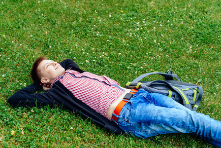 年轻的快乐男人的肖像，背包躺在绿草上，双手放在头下，享受大自然的复制空间