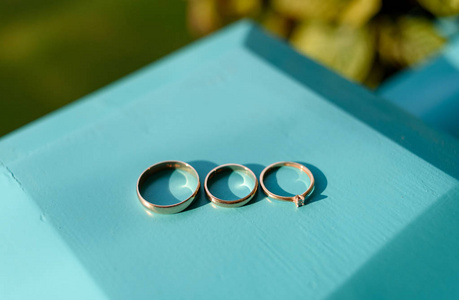 三枚结婚戒指在绿松石木背景上选择性聚焦。 订婚戒指与钻石新娘戒指和新郎戒指自由空间。 婚礼的配件。 求婚及婚礼概念