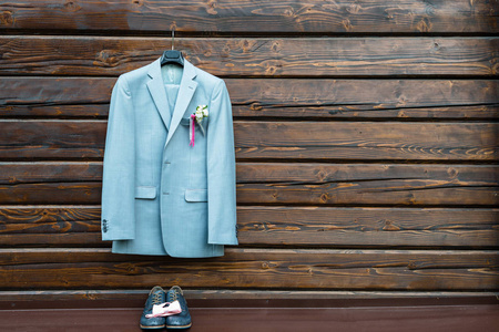 时尚优雅的婚礼新郎套装，扣眼挂在木制背景和复制空间。 灰色西装挂在皮鞋和粉红色的蝴蝶结上。 新郎婚礼配饰免费空间