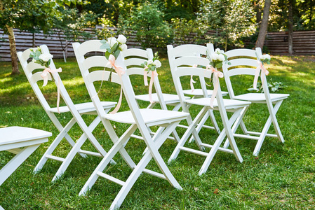 白色婚礼椅，每边的牌坊外脚复制空间与鲜花。 花园里绿草如茵的客人用空木椅准备举行婚礼