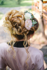 美丽的新娘穿着丝绸长袍，时尚的婚礼发型，鲜花背面。 金发女孩卷发造型。 长发发型