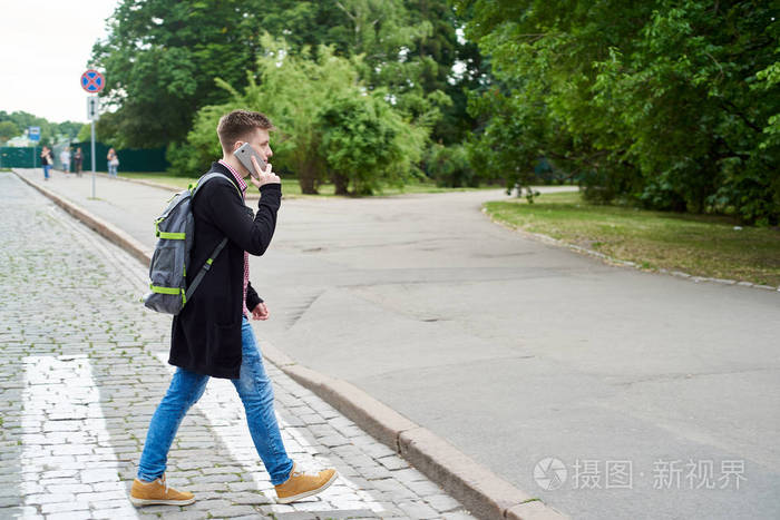 英俊的年轻人带着背包在手机上说话而在斑马自由空间过街游客沿着夏季