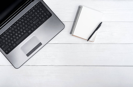 木制白色办公桌桌，开放空白笔记本电脑和空白日记与笔自由空间。 顶部视图与复制空间。 木制背景的灰色笔记本电脑