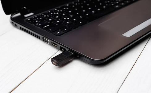 打开笔记本电脑与闪存驱动器在USB连接器白色木制背景特写。 现代笔记本和USB闪存的键盘。 将数据从闪存驱动器复制到笔记本。 封