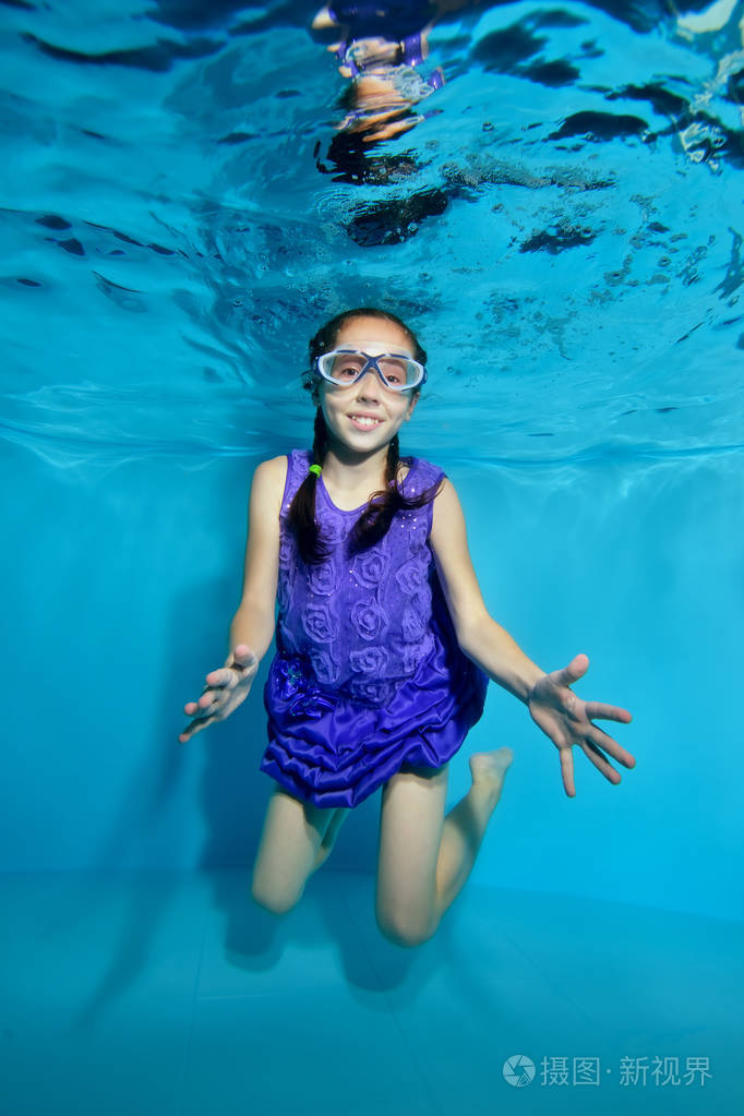 一个迷人的小女孩,扎着辫子,在游泳池里摆着姿势,微笑着,戴着蓝色的