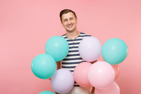 迷人的年轻快乐男人的肖像，穿着条纹T恤，手持五颜六色的气球，孤立在明亮的粉红色背景上。 人们真诚的情感生活方式观念。 广告区域