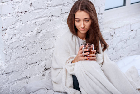 把漂亮的年轻女人关在温暖的格子里，手里拿着一杯热茶。 疾病和疾病。 生病的不健康的女性在室内喝温饮料。