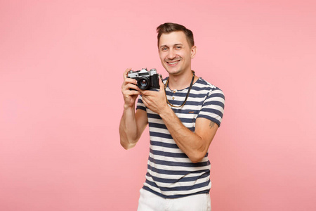 微笑的年轻摄影师的肖像，穿着条纹T恤，在复古复古照片相机上拍照，隔离在流行的粉彩背景上。 真诚的情感生活方式观念