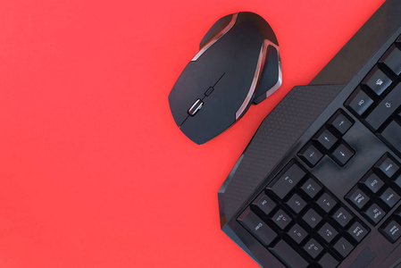 黑色鼠标键盘隔离在红色背景顶部视图上。 平躺游戏背景。 带有红色背景上的键盘和鼠标的工作区。 共用空间