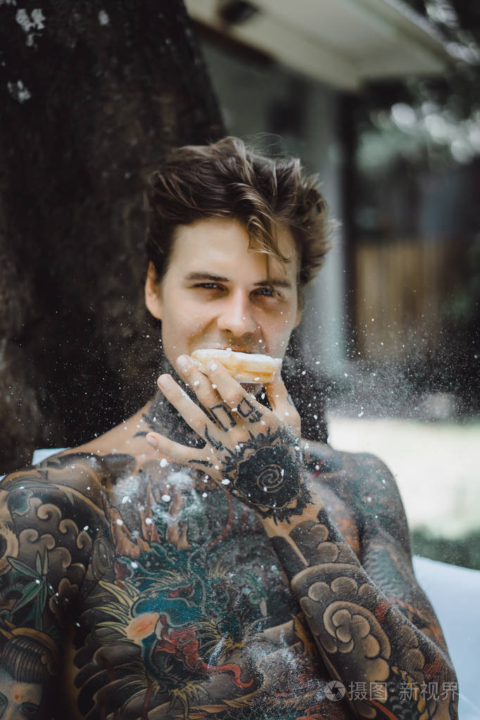 年轻英俊的纹身男在户外露天的床上吃早餐