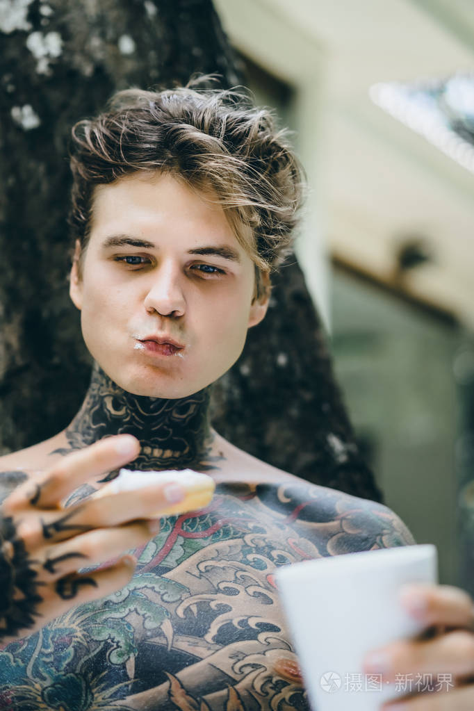 年轻英俊的纹身男在户外露天的床上吃早餐