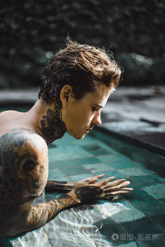 年轻的帅哥纹身在户外游泳池里休息。 游泳池里有个纹身的人玩得很开心。 印度尼西亚巴厘岛