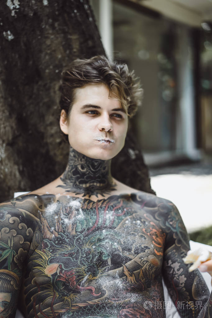 年轻英俊的纹身男在户外露天的床上吃早餐