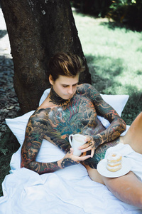 年轻英俊的纹身男在户外露天的床上吃早餐