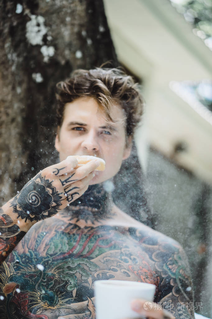 年轻英俊的纹身男在户外露天的床上吃早餐