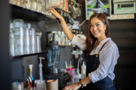 亚洲女性咖啡师微笑着在咖啡店柜台使用咖啡机，工作妇女，小企业主，食物和饮料咖啡馆的概念